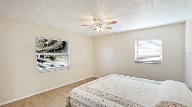 bedroom with light wood-style flooring, a ceiling fan, baseboards, and a textured ceiling