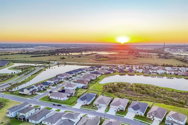 aerial view at dusk featuring a residential view and a water view