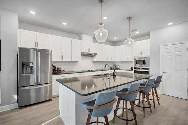 kitchen with dark countertops, under cabinet range hood, light wood-style floors, stainless steel appliances, and a sink