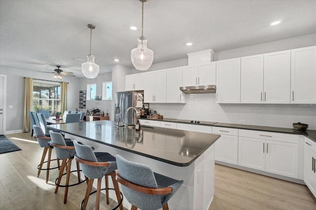 kitchen featuring stainless steel refrigerator with ice dispenser, under cabinet range hood, a sink, dark countertops, and black electric stovetop