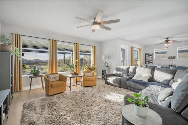 living area featuring bar, baseboards, light wood-style floors, and ceiling fan