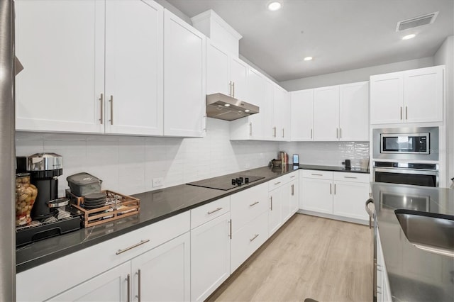 kitchen featuring visible vents, backsplash, under cabinet range hood, light wood-style flooring, and appliances with stainless steel finishes