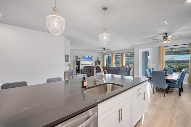 kitchen with hanging light fixtures, dark countertops, a ceiling fan, and a sink