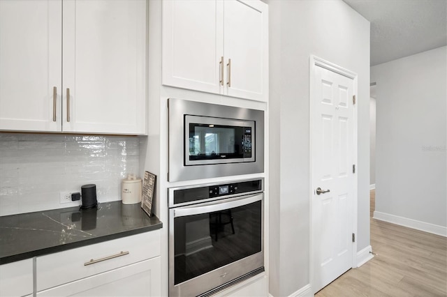 kitchen with dark countertops, backsplash, light wood-style floors, white cabinets, and stainless steel appliances