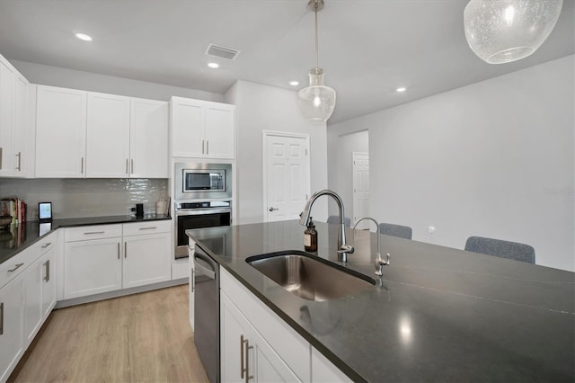 kitchen featuring dark countertops, visible vents, appliances with stainless steel finishes, light wood-style floors, and a sink