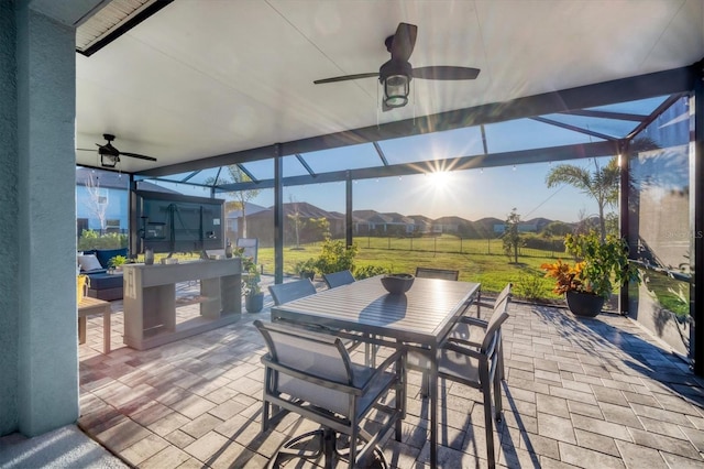 view of patio featuring outdoor dining area, ceiling fan, and glass enclosure