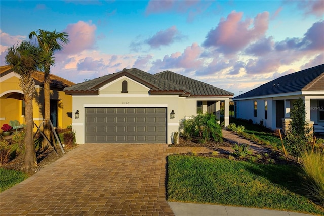 view of front facade with stucco siding, a tiled roof, decorative driveway, and a garage