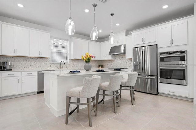 kitchen with under cabinet range hood, appliances with stainless steel finishes, white cabinetry, and a center island