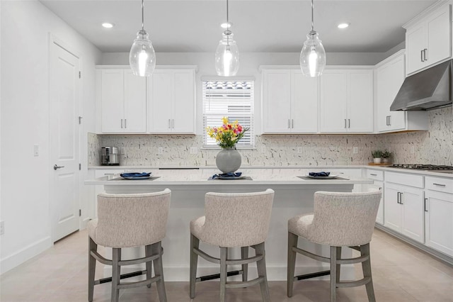 kitchen with under cabinet range hood, a kitchen bar, a center island, and white cabinetry