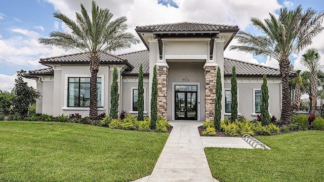 mediterranean / spanish-style house featuring stucco siding, a front lawn, french doors, stone siding, and a tile roof