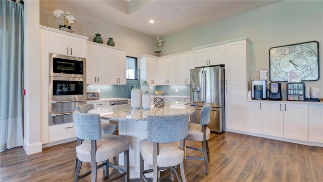 kitchen featuring a kitchen island, white cabinets, appliances with stainless steel finishes, a kitchen breakfast bar, and tasteful backsplash