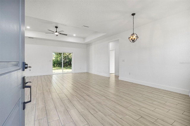 unfurnished room featuring baseboards, a tray ceiling, recessed lighting, light wood-style flooring, and ceiling fan with notable chandelier