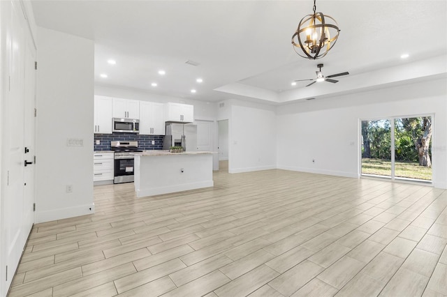 kitchen with tasteful backsplash, open floor plan, a tray ceiling, stainless steel appliances, and white cabinetry