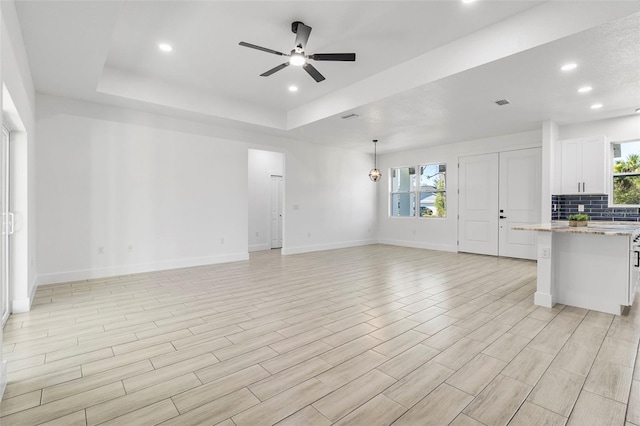 unfurnished living room featuring recessed lighting, baseboards, a raised ceiling, and a ceiling fan