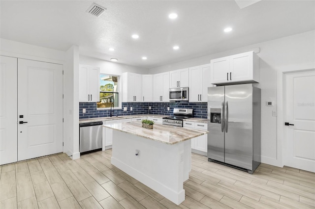 kitchen with a sink, decorative backsplash, white cabinets, appliances with stainless steel finishes, and a center island