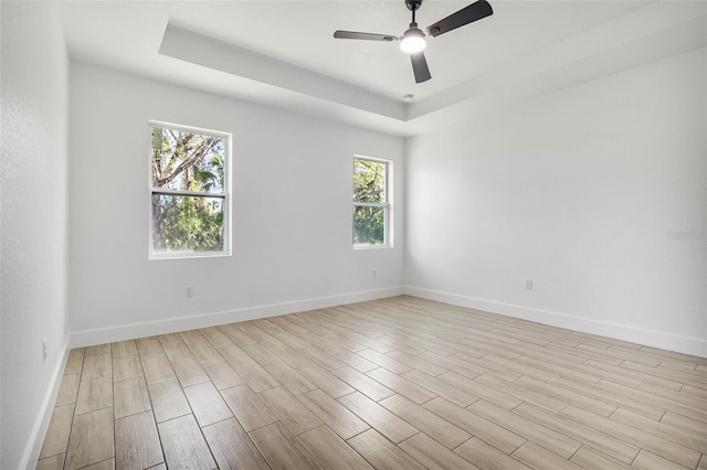 unfurnished room with a tray ceiling, baseboards, light wood finished floors, and ceiling fan