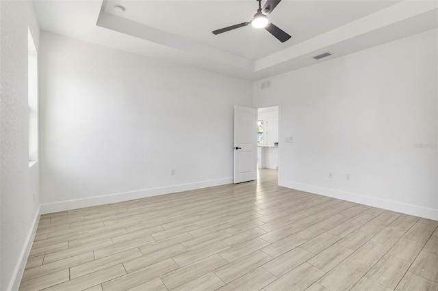 unfurnished room with visible vents, baseboards, light wood-type flooring, a tray ceiling, and a ceiling fan