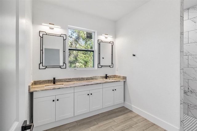 bathroom with baseboards, wood finish floors, tiled shower, double vanity, and a sink