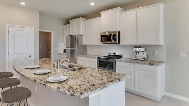 kitchen with a center island with sink, a breakfast bar, appliances with stainless steel finishes, white cabinetry, and a sink