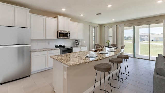 kitchen featuring visible vents, a center island with sink, decorative backsplash, stainless steel appliances, and a sink