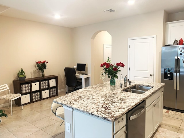 kitchen featuring light stone countertops, arched walkways, white cabinets, stainless steel appliances, and a sink