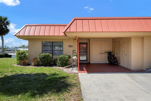 view of front of property featuring a front lawn, concrete driveway, stucco siding, a carport, and a standing seam roof