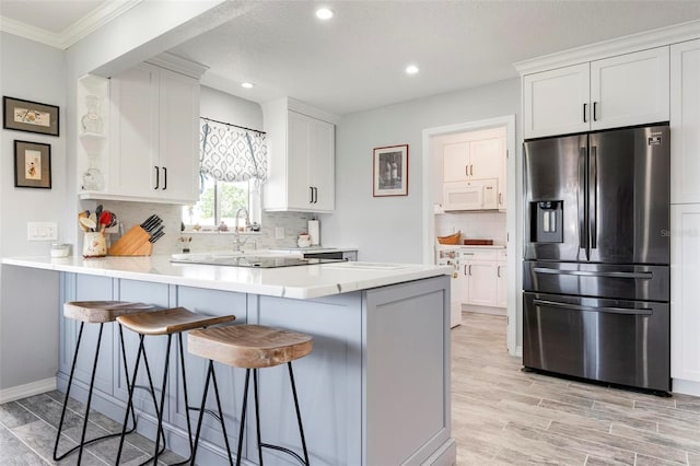 kitchen featuring white microwave, a peninsula, a breakfast bar, and stainless steel refrigerator with ice dispenser