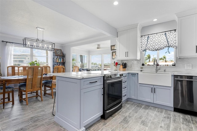 kitchen with wood tiled floor, a peninsula, a sink, light countertops, and appliances with stainless steel finishes