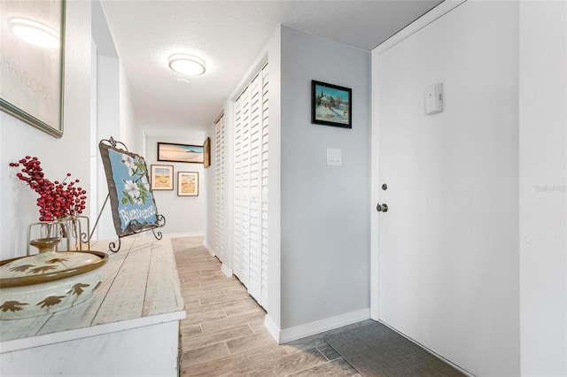 corridor with baseboards, a textured ceiling, and wood tiled floor