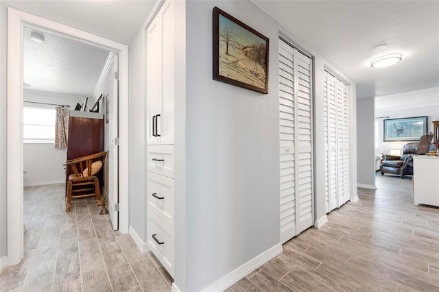 hallway featuring wood tiled floor, baseboards, and a textured ceiling