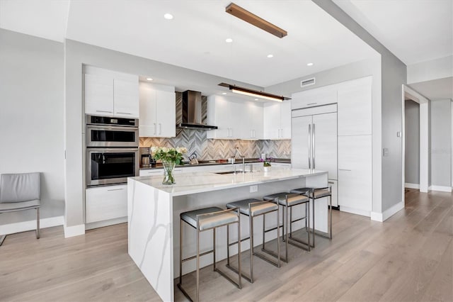 kitchen with double oven, built in refrigerator, white cabinetry, wall chimney exhaust hood, and modern cabinets