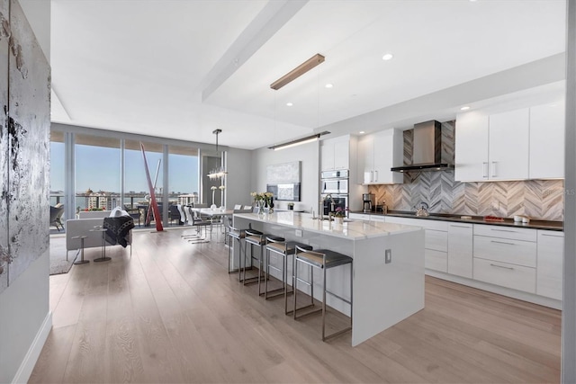 kitchen featuring a breakfast bar area, decorative backsplash, white cabinets, modern cabinets, and wall chimney exhaust hood