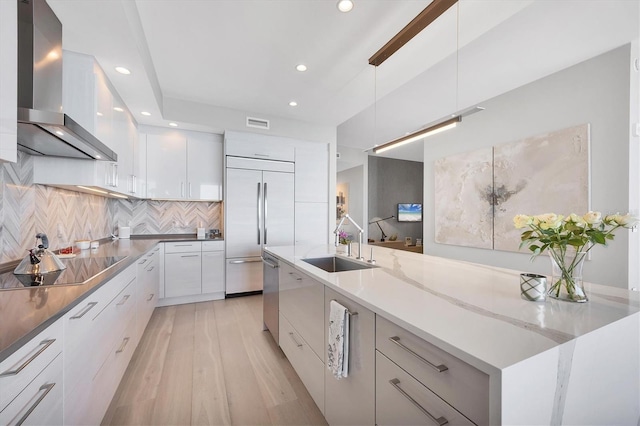 kitchen with wall chimney exhaust hood, modern cabinets, built in refrigerator, and a sink