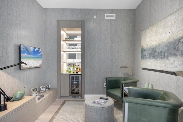 living area with visible vents, light wood finished floors, wallpapered walls, a bar, and wine cooler