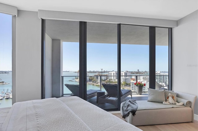 bedroom featuring expansive windows, a water view, wood finished floors, and a view of city