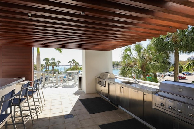 view of patio / terrace with a sink, a water view, area for grilling, and exterior kitchen