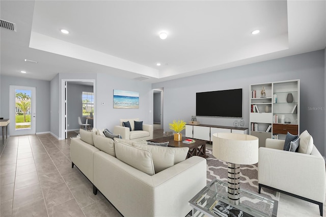 living area with a tray ceiling, recessed lighting, visible vents, and baseboards