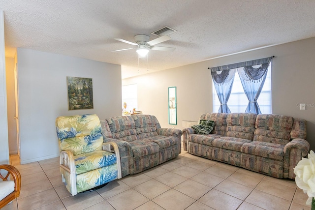 living room featuring light tile patterned floors, visible vents, a textured ceiling, and a ceiling fan