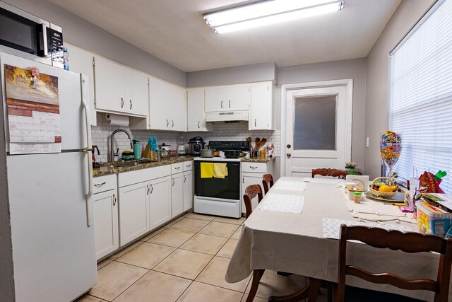 kitchen featuring electric range, light tile patterned flooring, freestanding refrigerator, a sink, and under cabinet range hood