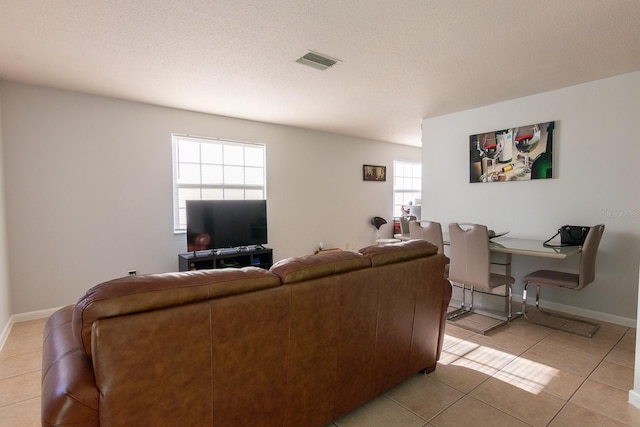 living area featuring light tile patterned floors, baseboards, visible vents, and a textured ceiling