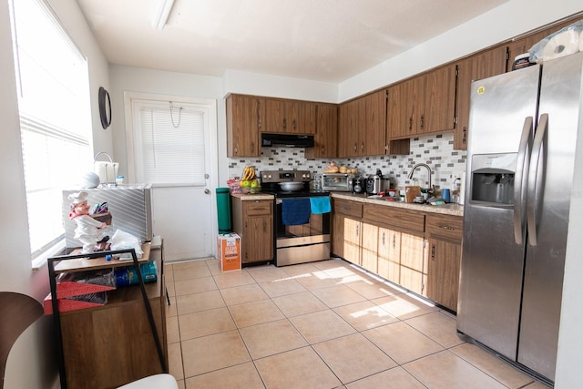 kitchen featuring a sink, decorative backsplash, light countertops, under cabinet range hood, and appliances with stainless steel finishes