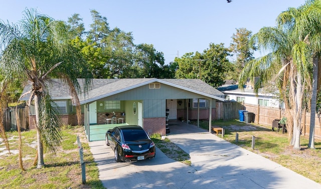 view of front of house with an attached carport, brick siding, driveway, and fence