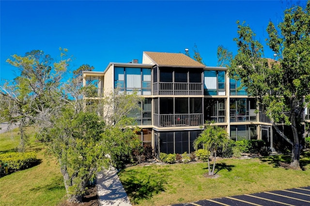 rear view of property featuring uncovered parking, a lawn, and a sunroom