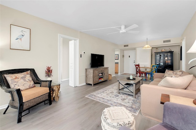 living area featuring visible vents, baseboards, light wood-style floors, and ceiling fan