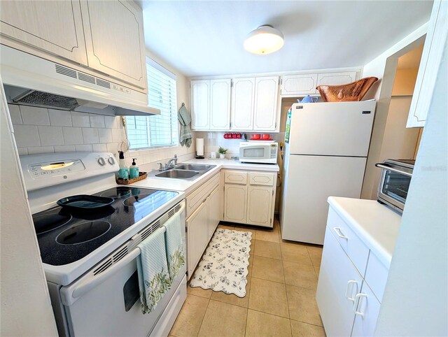 kitchen featuring tasteful backsplash, under cabinet range hood, light tile patterned flooring, white appliances, and a sink