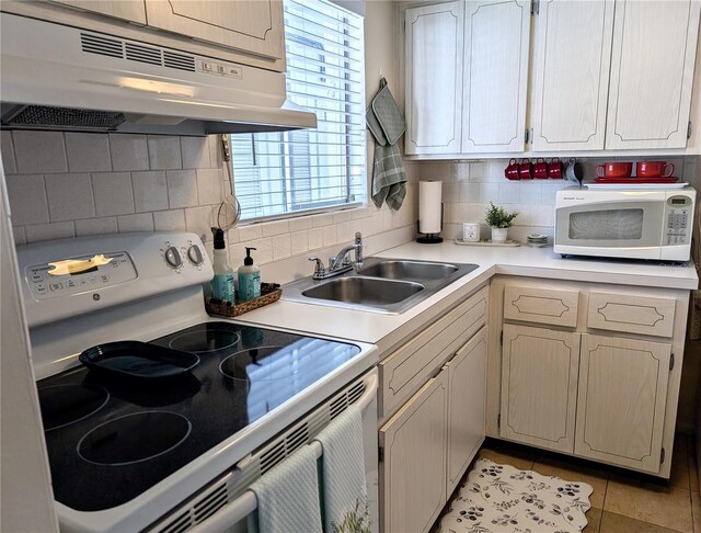 kitchen featuring white appliances, a sink, light countertops, under cabinet range hood, and tasteful backsplash