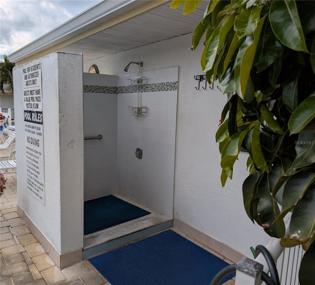 full bath with brick floor, baseboards, and tiled shower