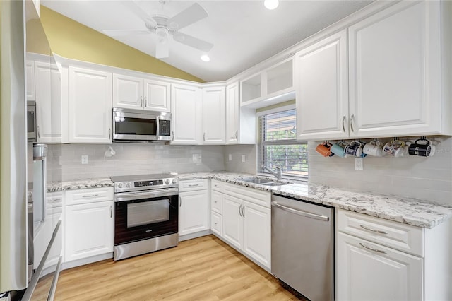 kitchen with stainless steel appliances, light wood-style flooring, vaulted ceiling, white cabinetry, and decorative backsplash