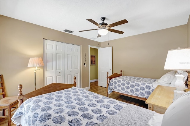 bedroom with wood finished floors, visible vents, a closet, baseboards, and ceiling fan