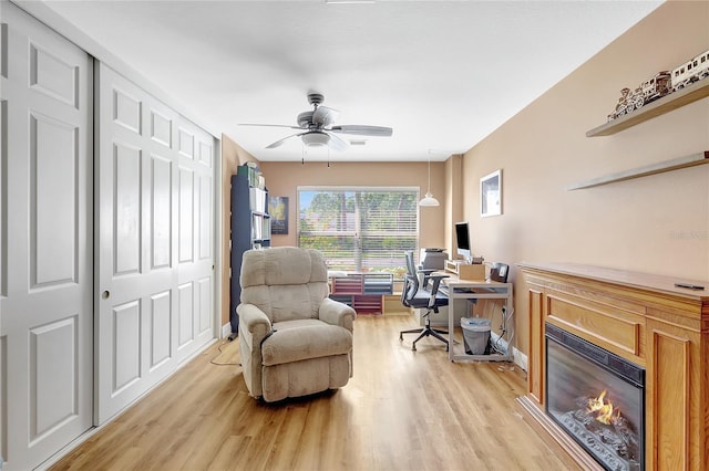 office with ceiling fan, baseboards, a glass covered fireplace, and light wood-style floors